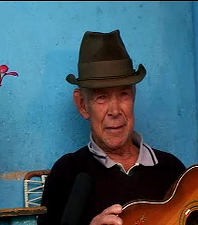 Moisés Vargas Turriago, Morei, con sombrero y su tiple, frente a la pared azul de su casa en Fómeque