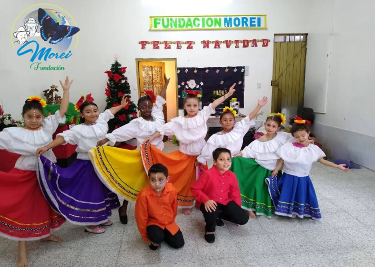 Niñas y niños de la Fundación Morei con trajes típicos de danza, en una sede decorada con el letrero «Feliz Navidad»